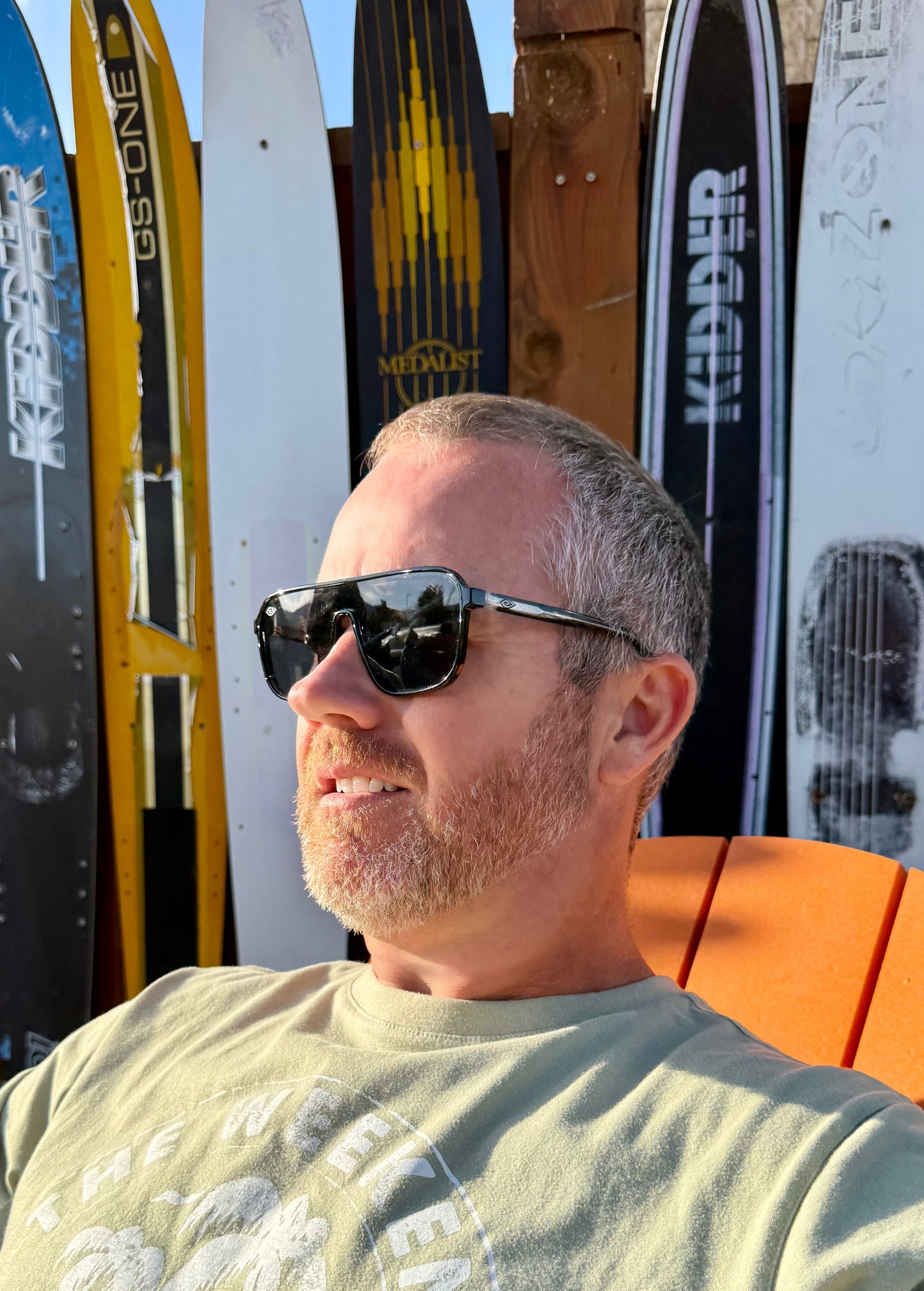 Man wearing sunglasses sitting in front of skis with visible brand names.